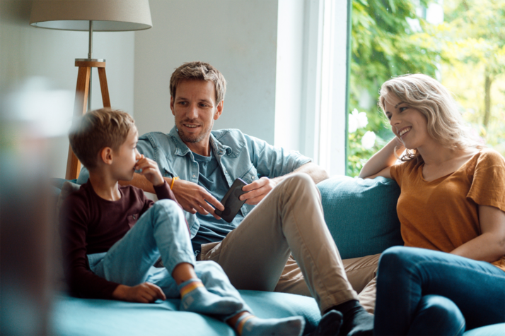 Familiendiskussion Vater, Mutter und Sohn sitzen auf der Couch und diskutieren über Handynutzung.